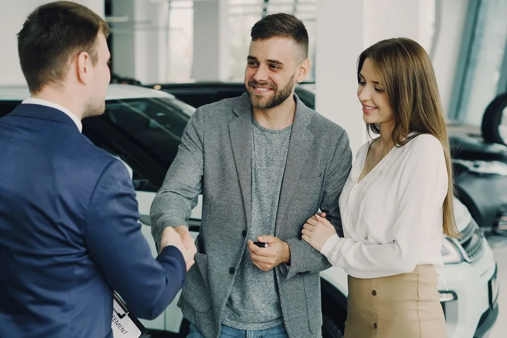 Couple shaking hands with a dealership finance manager after a no credit car loan approval